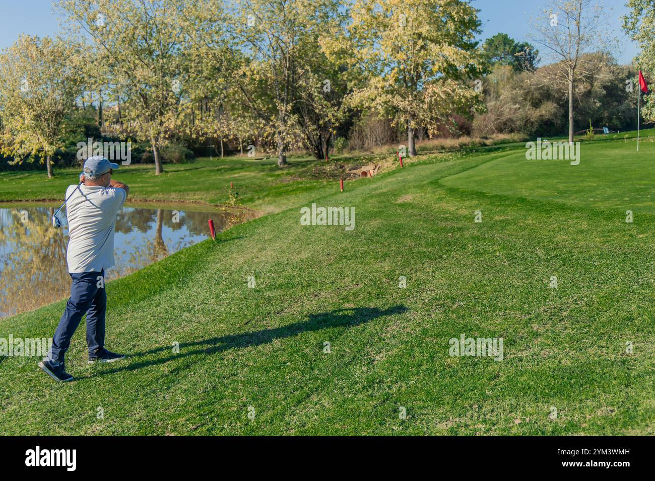 il golfista anziano dello spazio fa oscillare il suo club dal lungolago, puntando la palla verso la bandiera verde, dimostrando precisione e concentrazione sui campi da golf Foto Stock