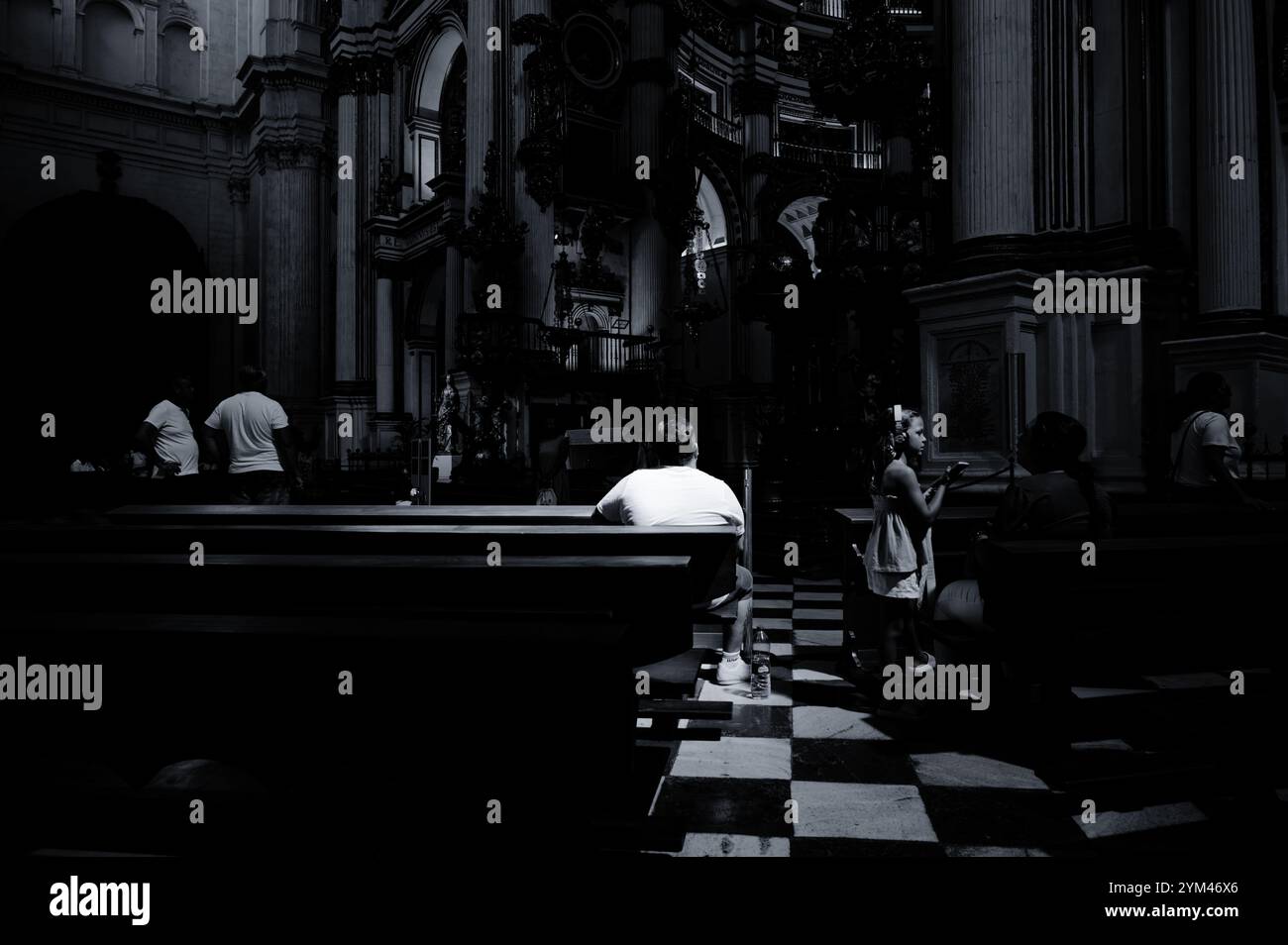 I visitatori all'interno della Cattedrale di Granada ammirano il suo intricato altare barocco, con la luce del sole che filtra attraverso, mettendo in risalto un credente Foto Stock