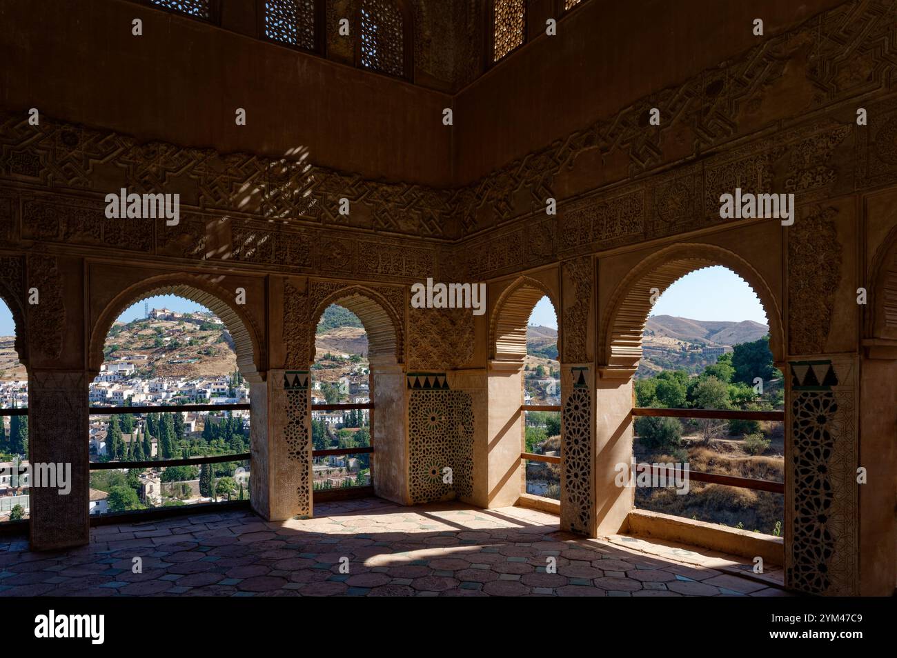 Gli intricati archi moreschi del Palazzo Partal dell'Alhambra incorniciano la vista delle colline e del verde di Granada sotto la luce del sole Foto Stock