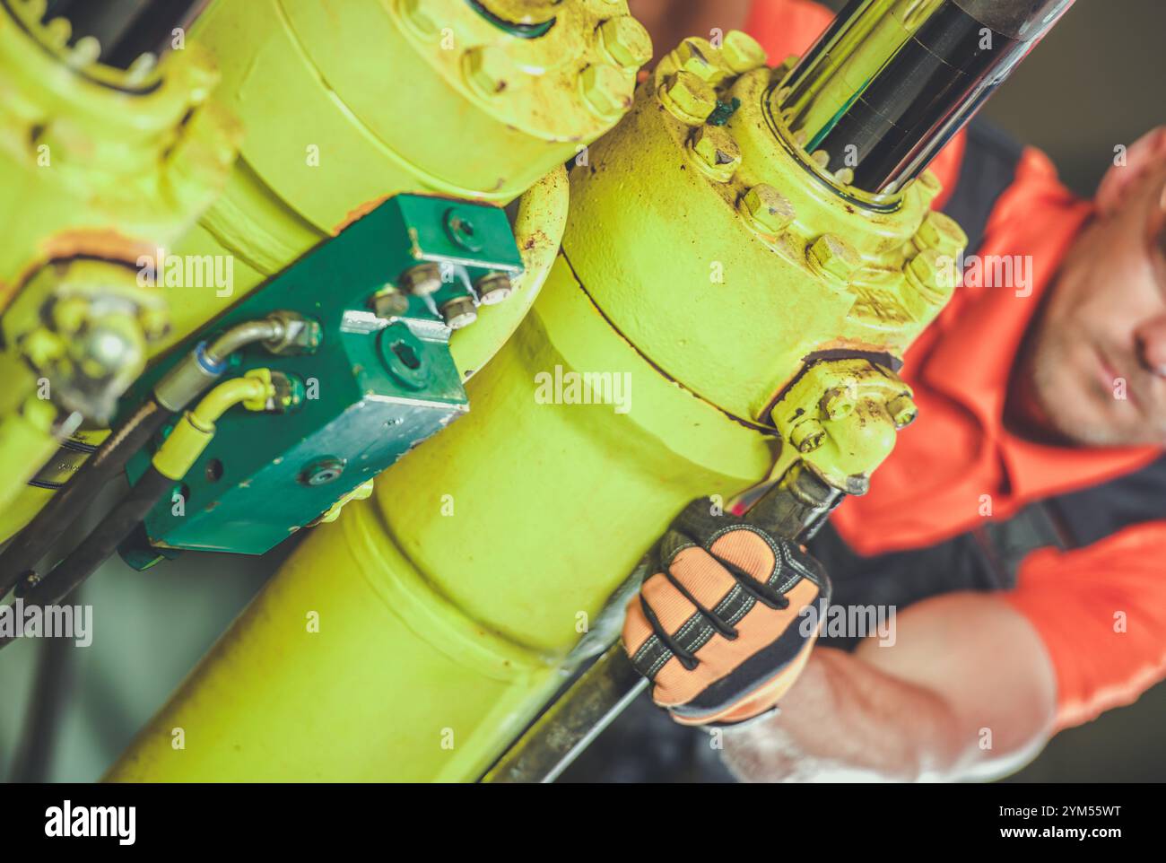 Un lavoratore si concentra sulla regolazione dei componenti dei macchinari idraulici utilizzando una chiave mentre si trova in un impianto industriale ben illuminato. Foto Stock