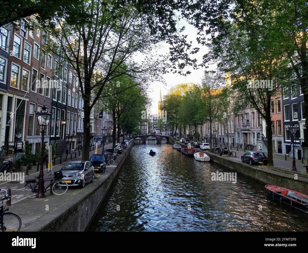 Vista sulla strada degli edifici che costeggiano un canale e della barca che transitano attraverso il canale di Amsterdam Foto Stock