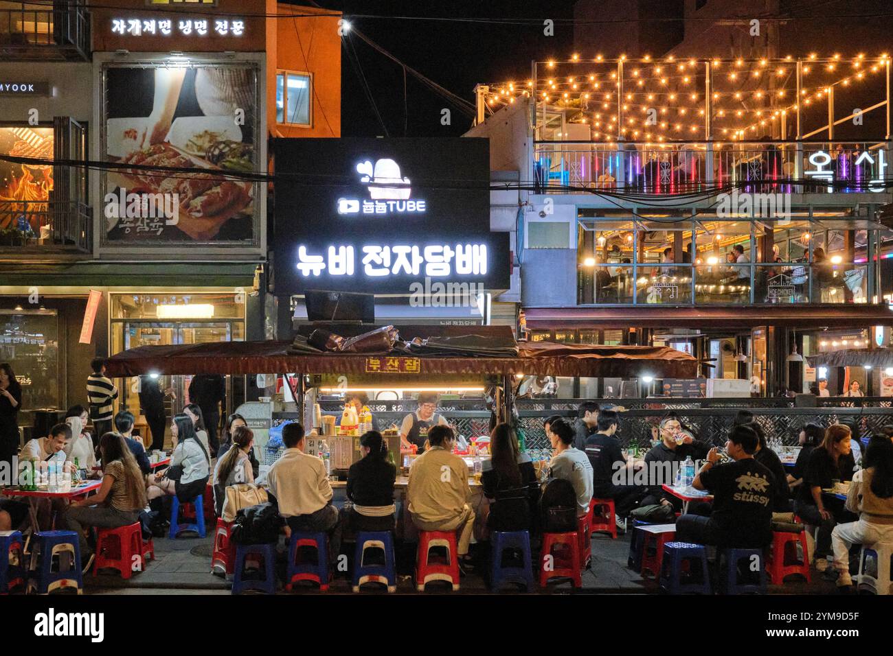 La gente apprezza il cibo di strada di notte nell'animata Jongno, Seoul, assaporando i sapori locali dalle vivaci bancarelle lungo la strada Foto Stock