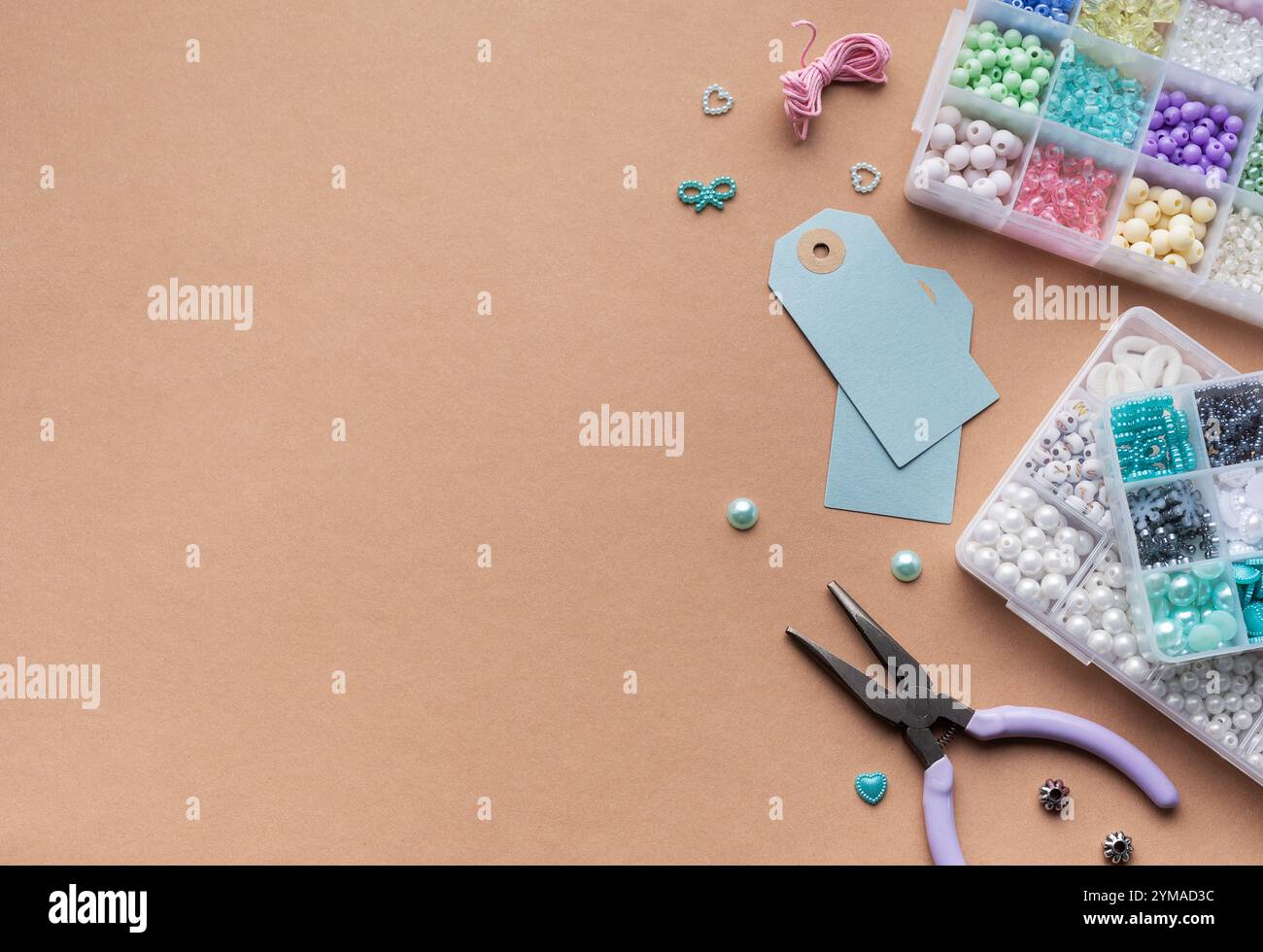Una configurazione piatta mette in mostra gli strumenti di creazione, tra cui pinze e cartellini blu, insieme a una serie di perline colorate disposte in scomparti, ideali per cr Foto Stock