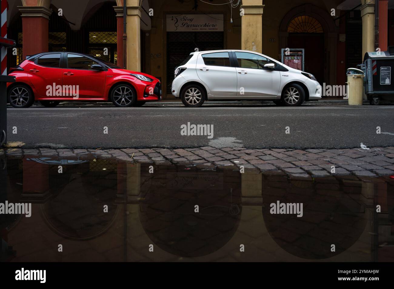 bologna, Italia. 9 ottobre 2024 - auto rosse e bianche parcheggiate sulla strada, con riflessi del famoso portico Foto Stock