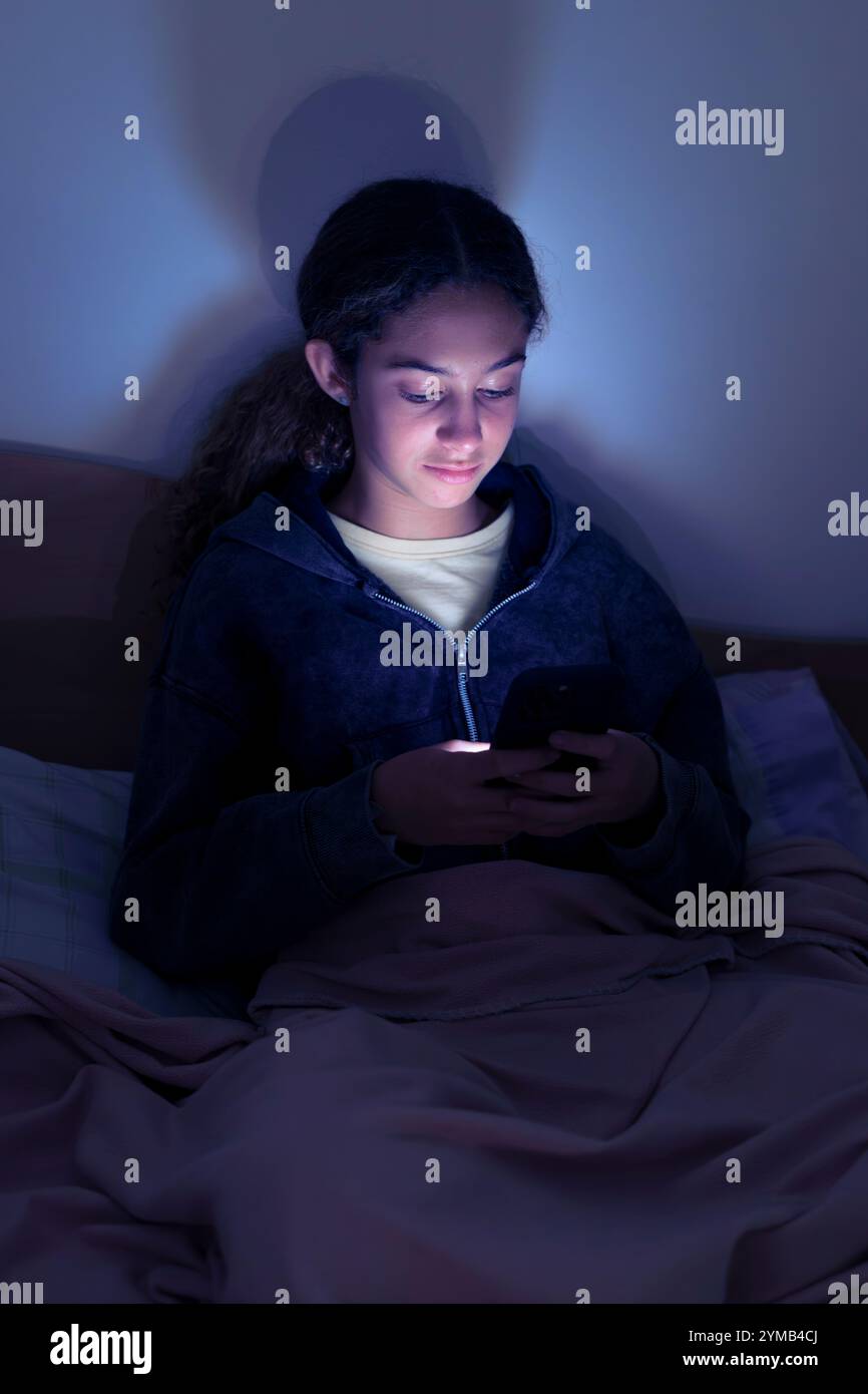 Teenager triste e stanca che usa uno smartphone sdraiato a letto a tarda notte, gioca, guarda video e digita. Dipendenza da schermo per bambini. SC Foto Stock