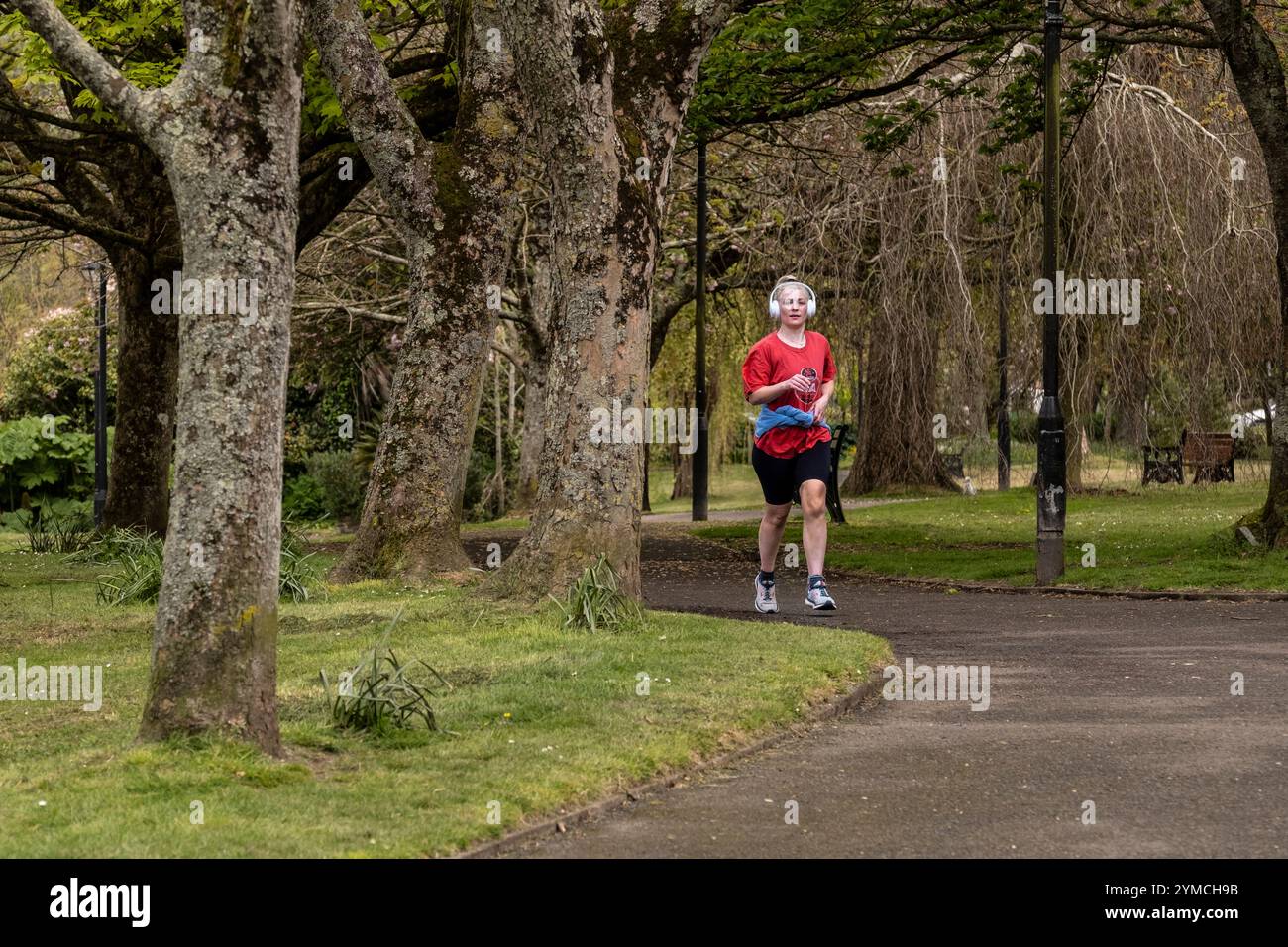 Una jogger runner che ascolta le sue cuffie mentre fa jogging attraverso i giardini Trenance di Newquay in Cornovaglia nel Regno Unito. Foto Stock