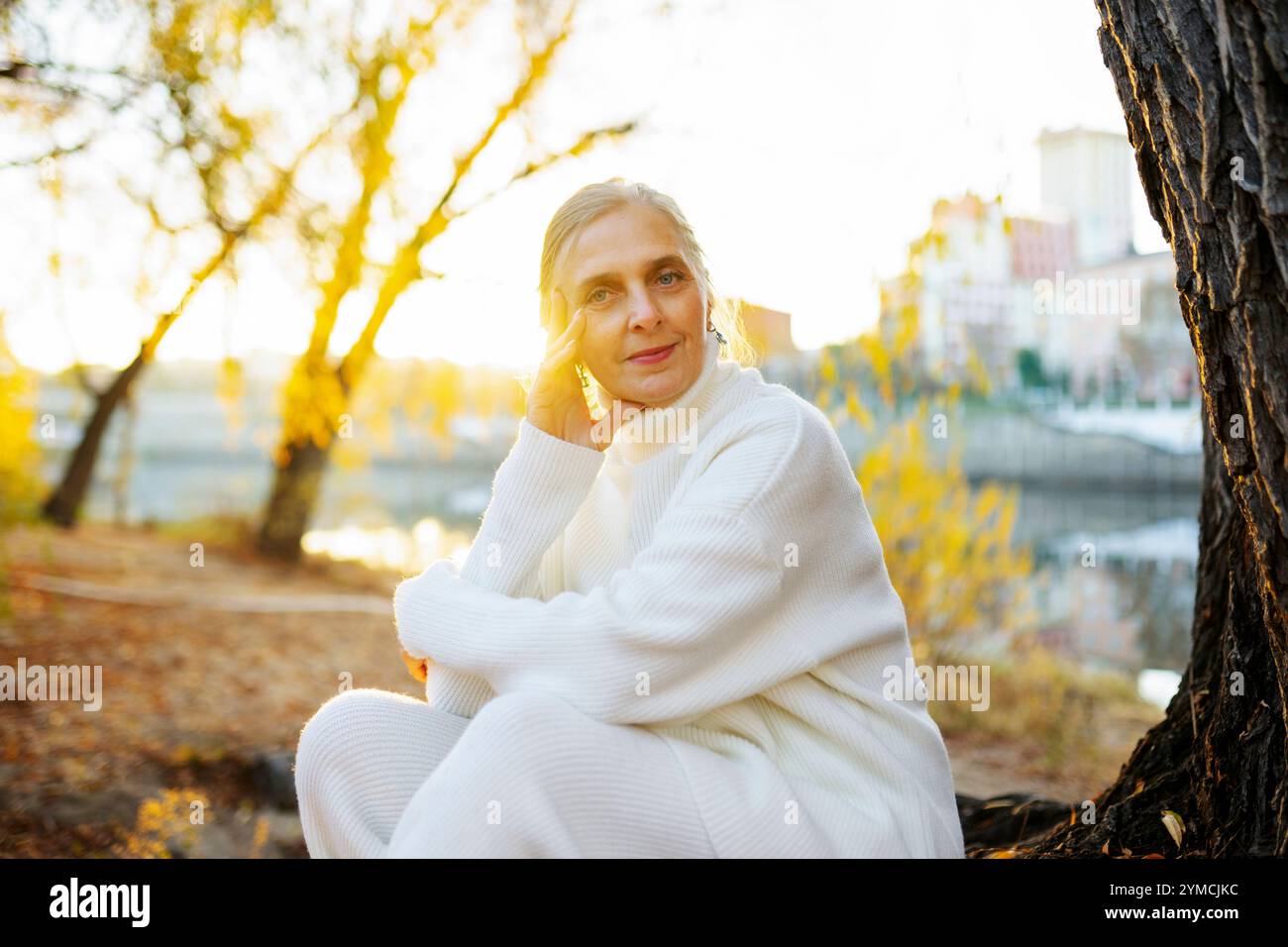 Ritratto di donna in maglione bianco seduta sul fiume in autunno Foto Stock