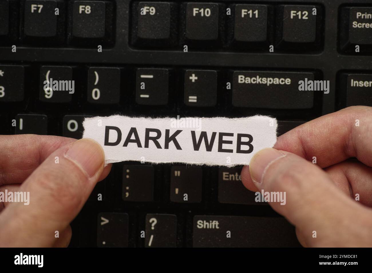 Un uomo che tiene un pezzo di carta con le parole Dark Web scritte tra le mani sopra una tastiera nera del computer coperta di polvere. Primo piano. Foto Stock