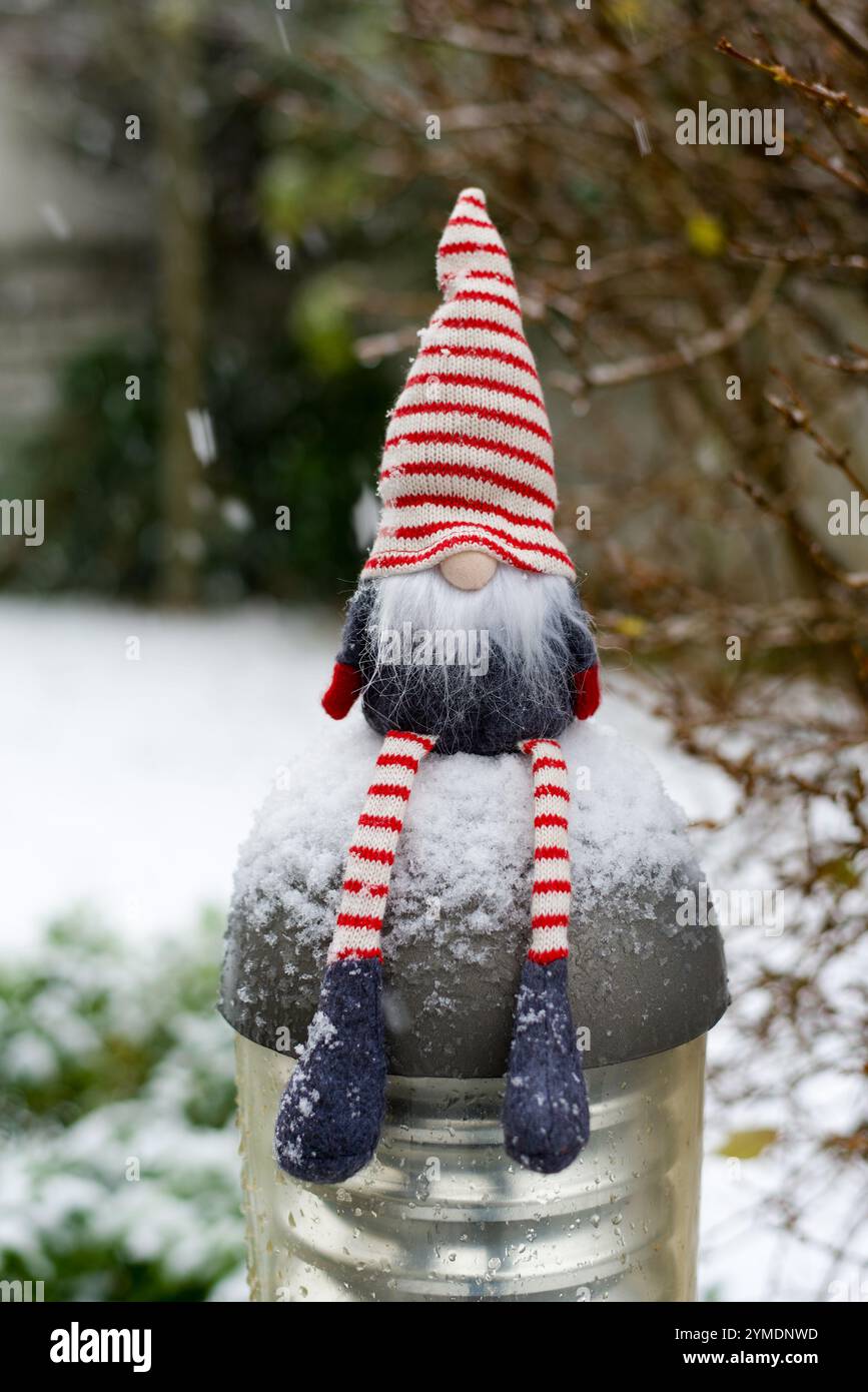 Una foto verticale di un simpatico gnomo natalizio seduto su una luce da giardino nella neve. Copia spazio. Foto Stock