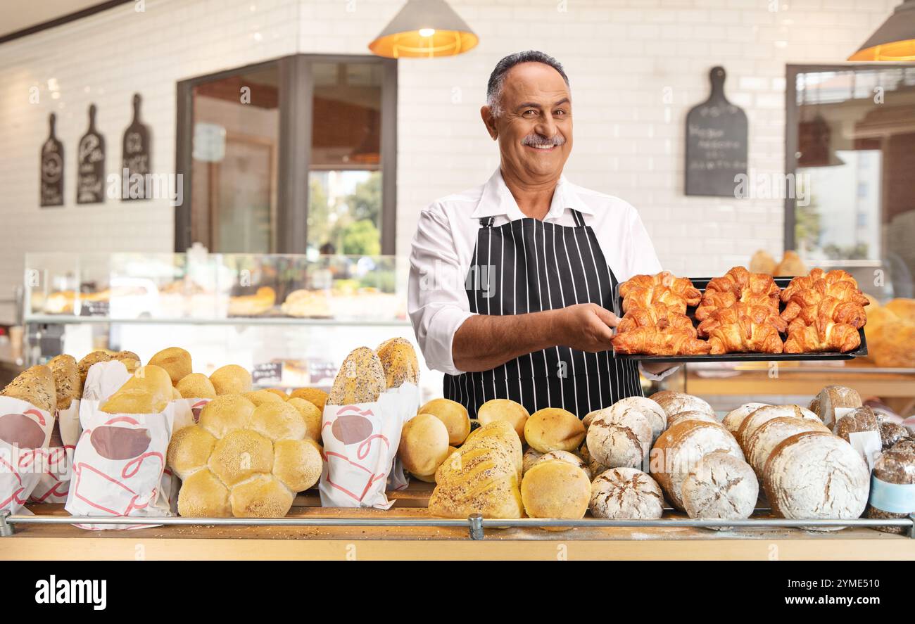 Uomo che tiene un vassoio con croissant all'interno di una panetteria Foto Stock