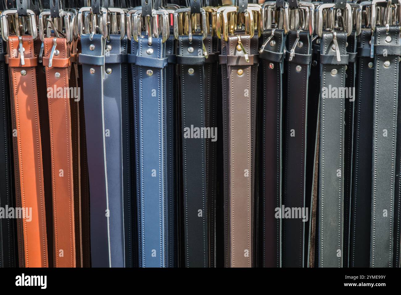Una fila di cinture pantaloni in pelle di diversi colori appese su un rack Foto Stock