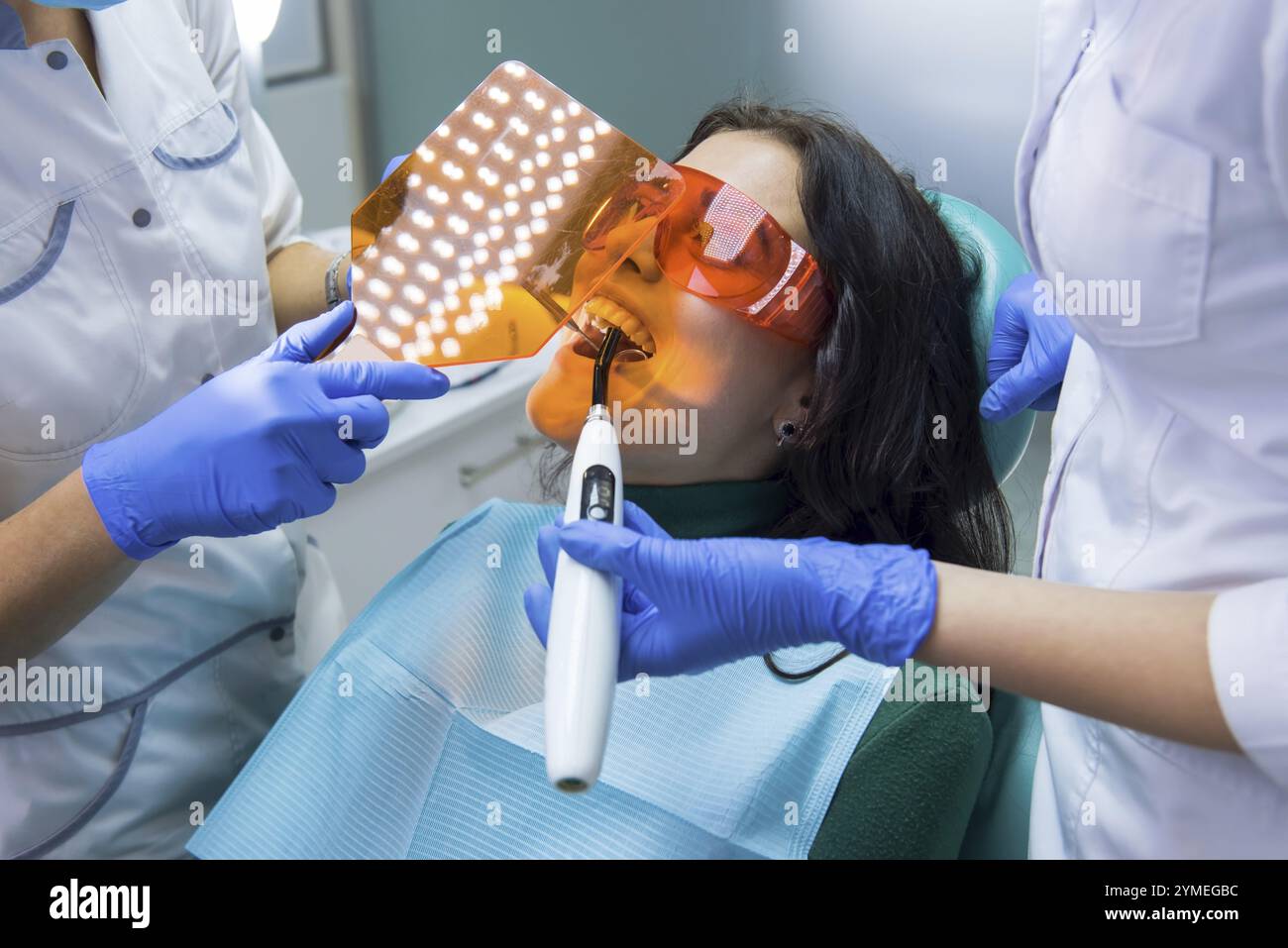 Il dentista sta sta usando la luce di indurimento. Giovane donna in poltrona dentale. Metodi efficaci e attrezzature moderne Foto Stock