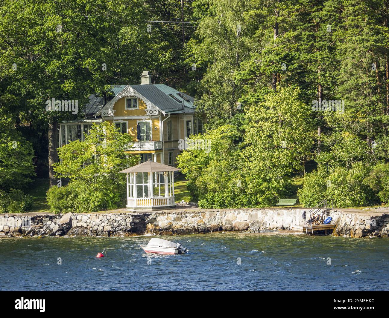 Casa gialla ai margini della foresta con una piccola barca sull'acqua, circondata da vegetazione lussureggiante, arcipelago, stoccolma, svezia Foto Stock