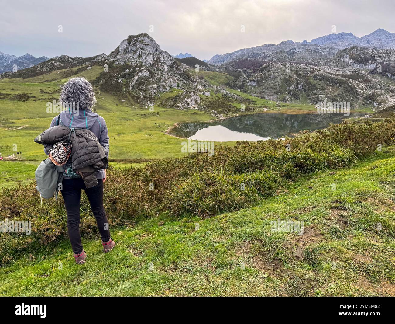 Donna dai capelli naturali ricci grigi che gode di una vista panoramica del lago Ercina e dei dintorni nel Parco Nazionale Picos de Europa, Asturie, Spagna - Immagine stock catturata con smartphone