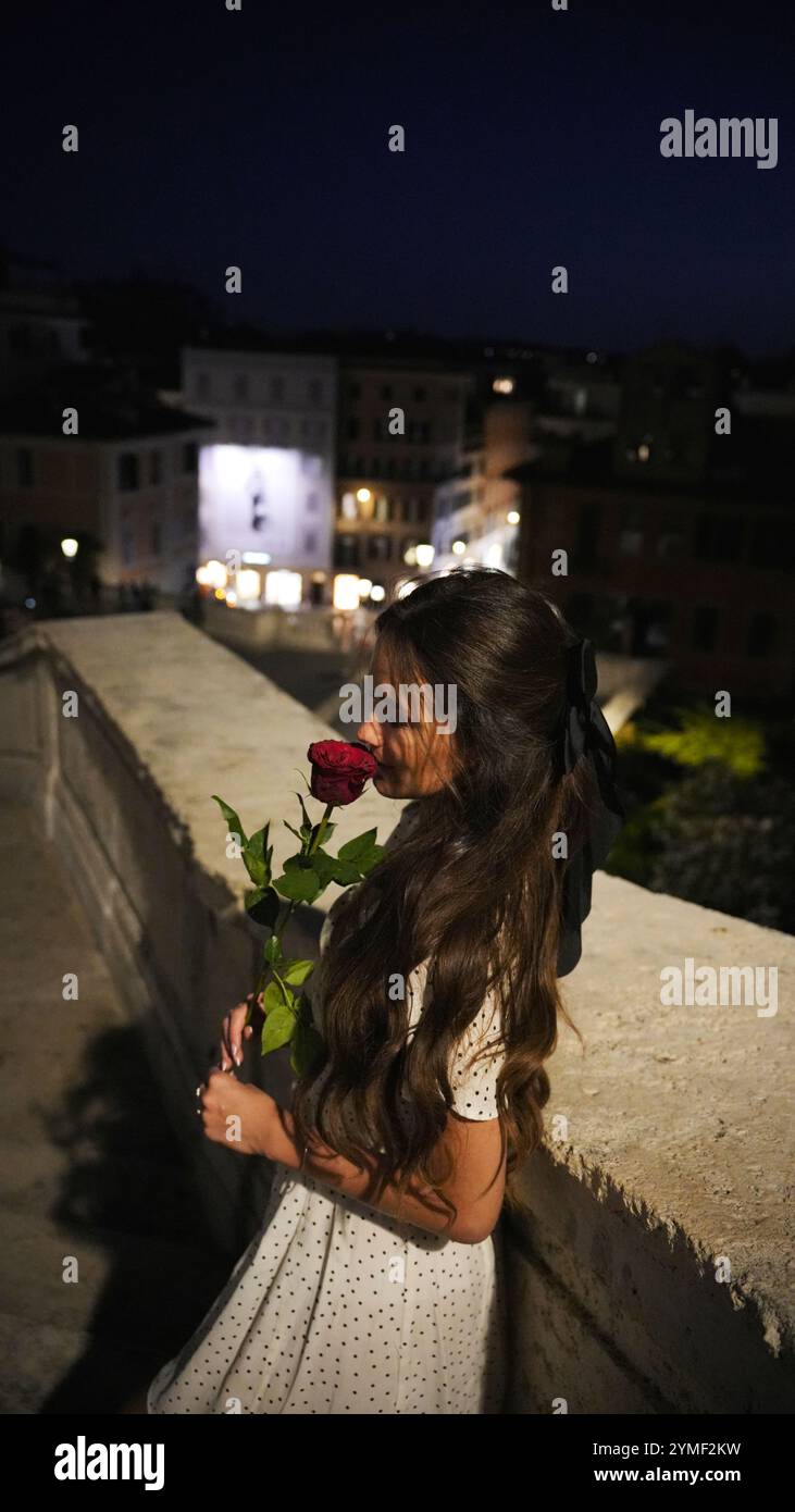 Serata romantica a Roma donna con rose rosse in abito a pois di notte Foto Stock