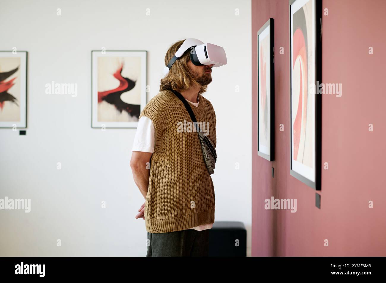 Uomo che partecipa a una mostra nella galleria d'arte indossando un visore per la realtà virtuale. Mostrare interesse per un'esperienza digitale immersiva migliorando l'apprezzamento delle opere d'arte Foto Stock