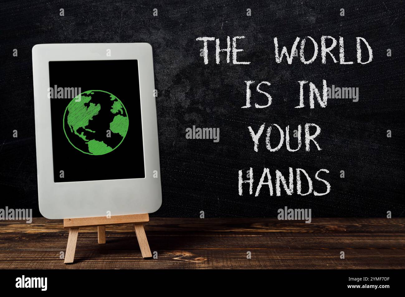Il tablet con un globo verde si trova su un piedistallo di legno. La tavoletta è su una lavagna nera con le parole che il mondo è nelle tue mani Foto Stock