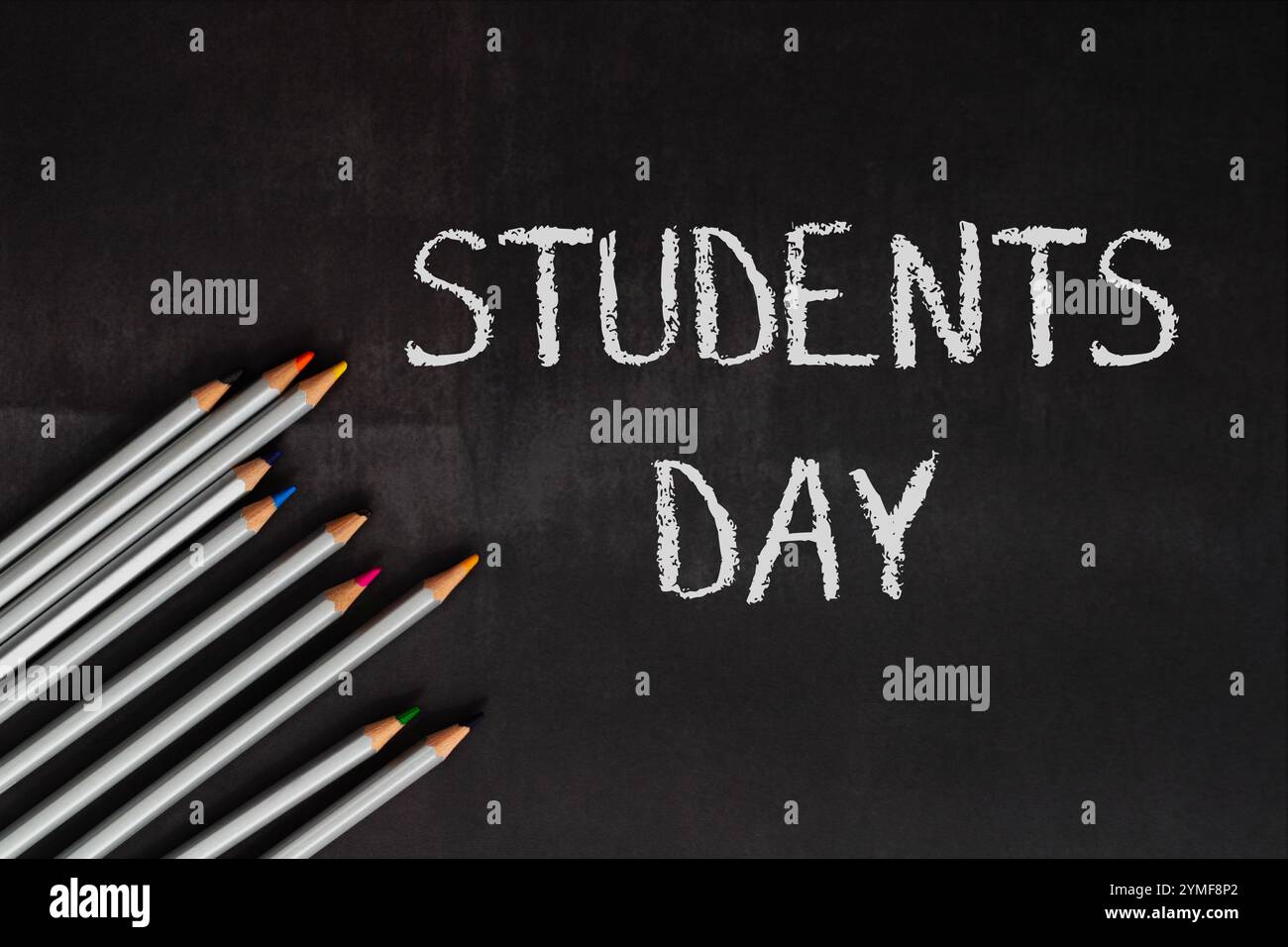 Il giorno degli studenti è scritto su una lavagna con un mucchio di matite sopra. Le matite sono disposte in fila e sono di colori diversi Foto Stock