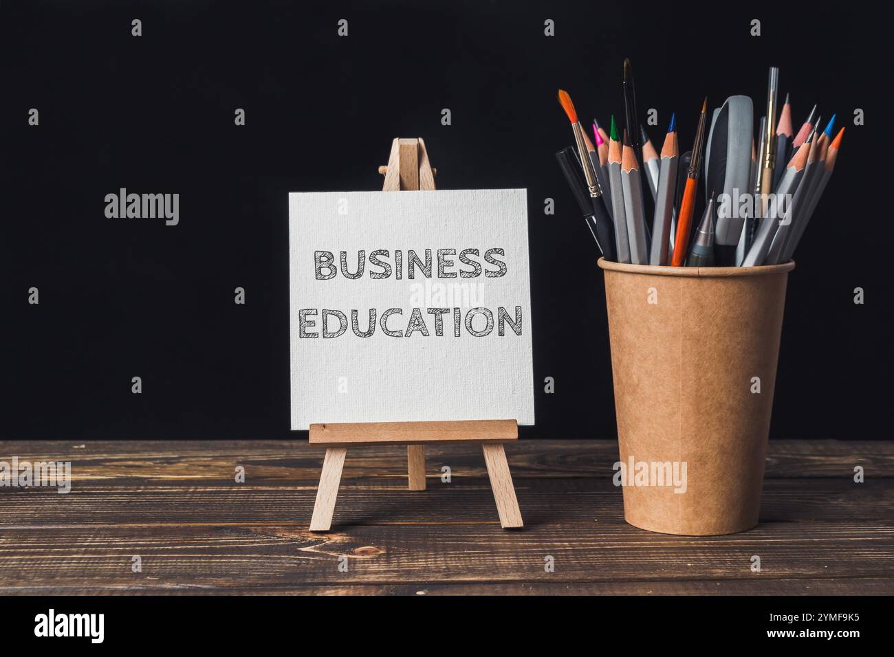 Una lavagna bianca con le parole "business Education" scritte sopra. Un cavalletto di legno regge il tabellone. Una tazza di matite colorate è seduta su un tavolo nex Foto Stock