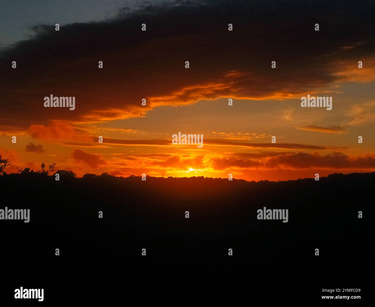 Panorama serale: Il rosso del sole che tramonta tra nuvole scure e orizzonte. Scena del tramonto: Esplosione di colori caldi e contrasti naturali. Foto Stock