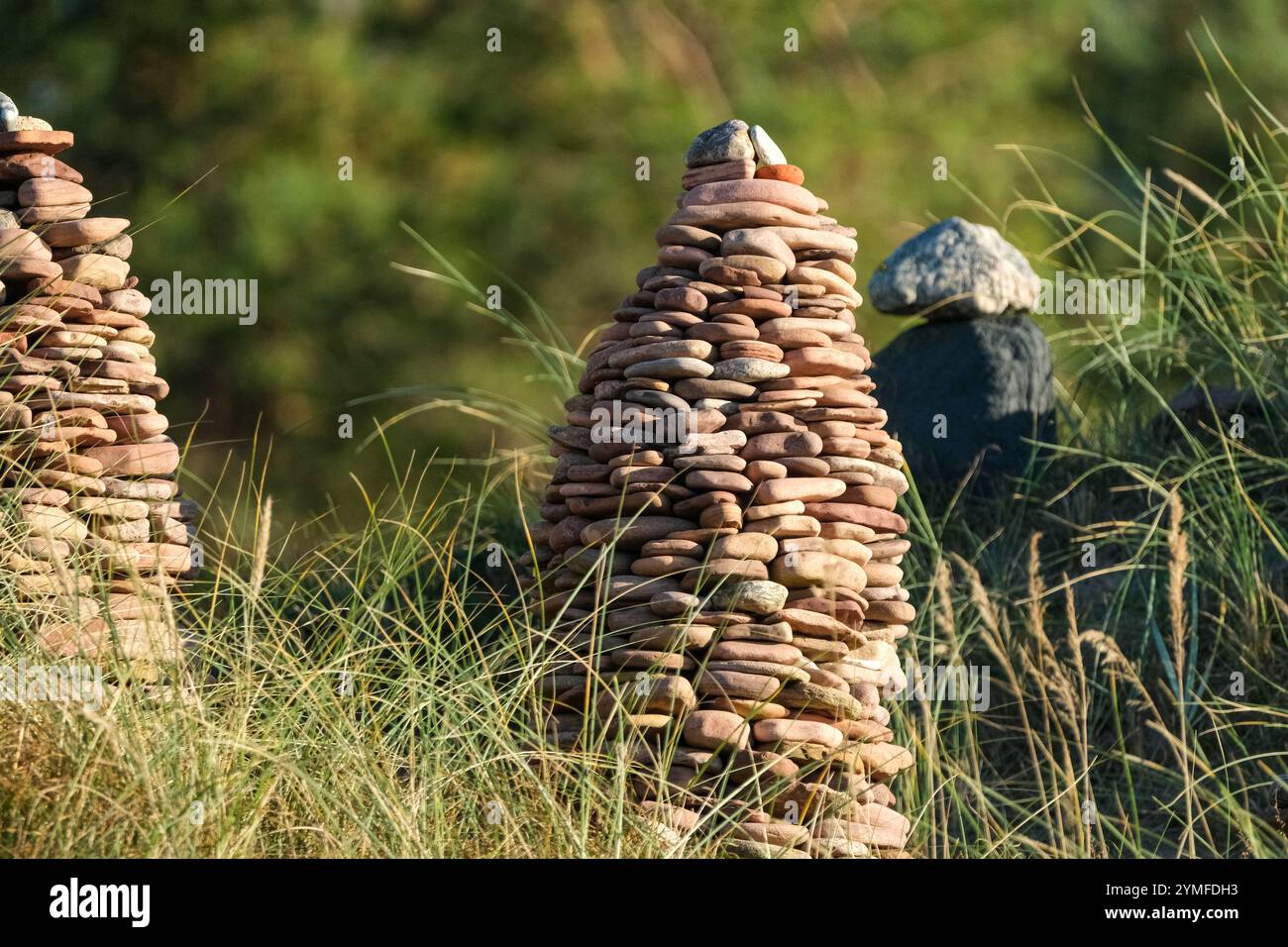 Primo piano di una torre di ciottoli accuratamente impilata in un'area costiera erbosa, con vegetazione naturale offuscata sullo sfondo. Foto Stock