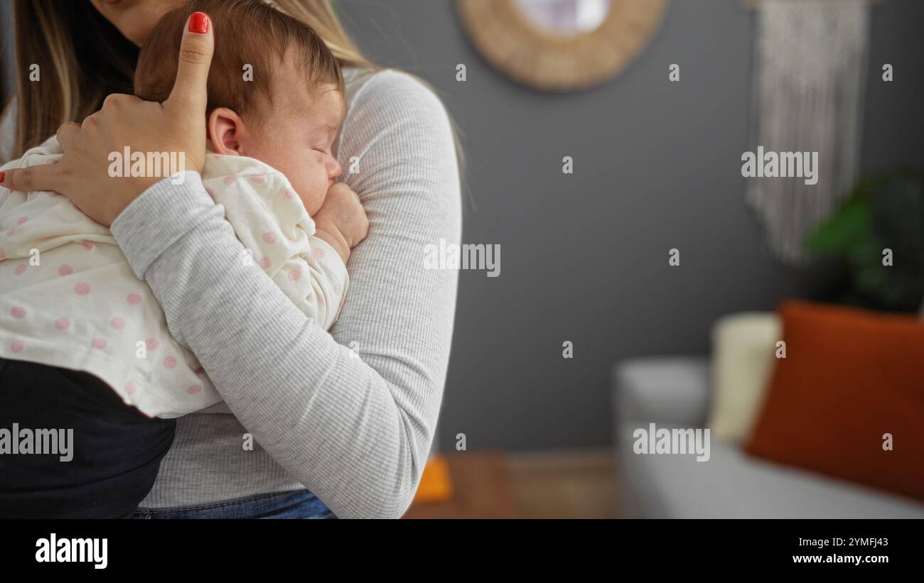 Donna che tiene il bambino in un abbraccio amorevole a casa in un accogliente soggiorno con arredi caldi, che enfatizza il legame familiare e il comfort. Foto Stock