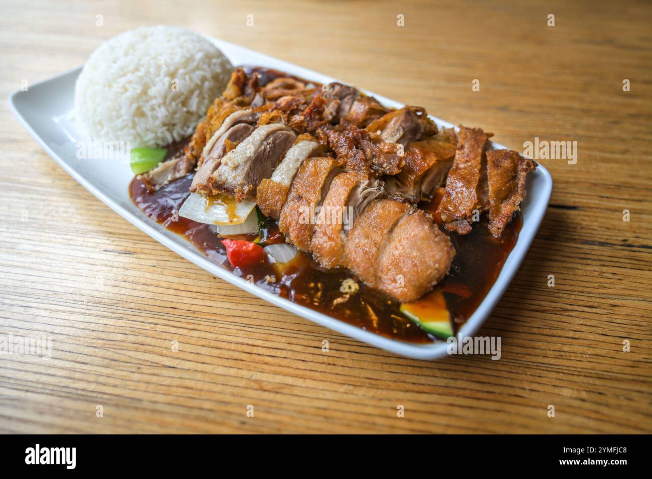 Croccanti fette di anatra arrosto sulle verdure con salsa e riso servite su un piatto quadrato bianco su un tavolo di legno in un ristorante cinese, spazio copia, sel Foto Stock
