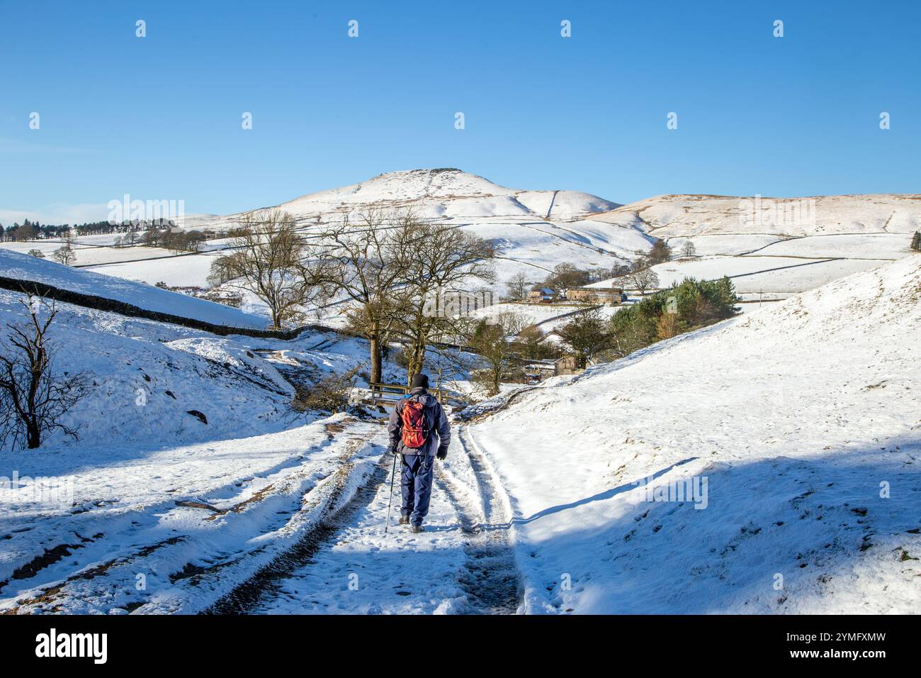 Uomo che cammina da solo con lo zaino in spalla in un paesaggio invernale innevato del Cheshire Peak District nel ruscello di Cumberland, Wildboarclough, verso Shutlingsloe Hill Foto Stock