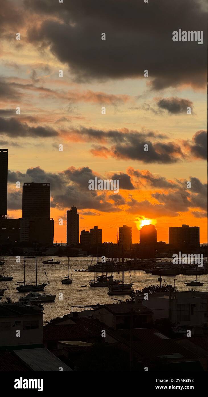 Tramonto vibrante su un porto, con alti edifici che delineano lo skyline e barche all'ancora. Perfetto per paesaggi, turismo e destinazioni costiere - Immagine stock catturata con smartphone