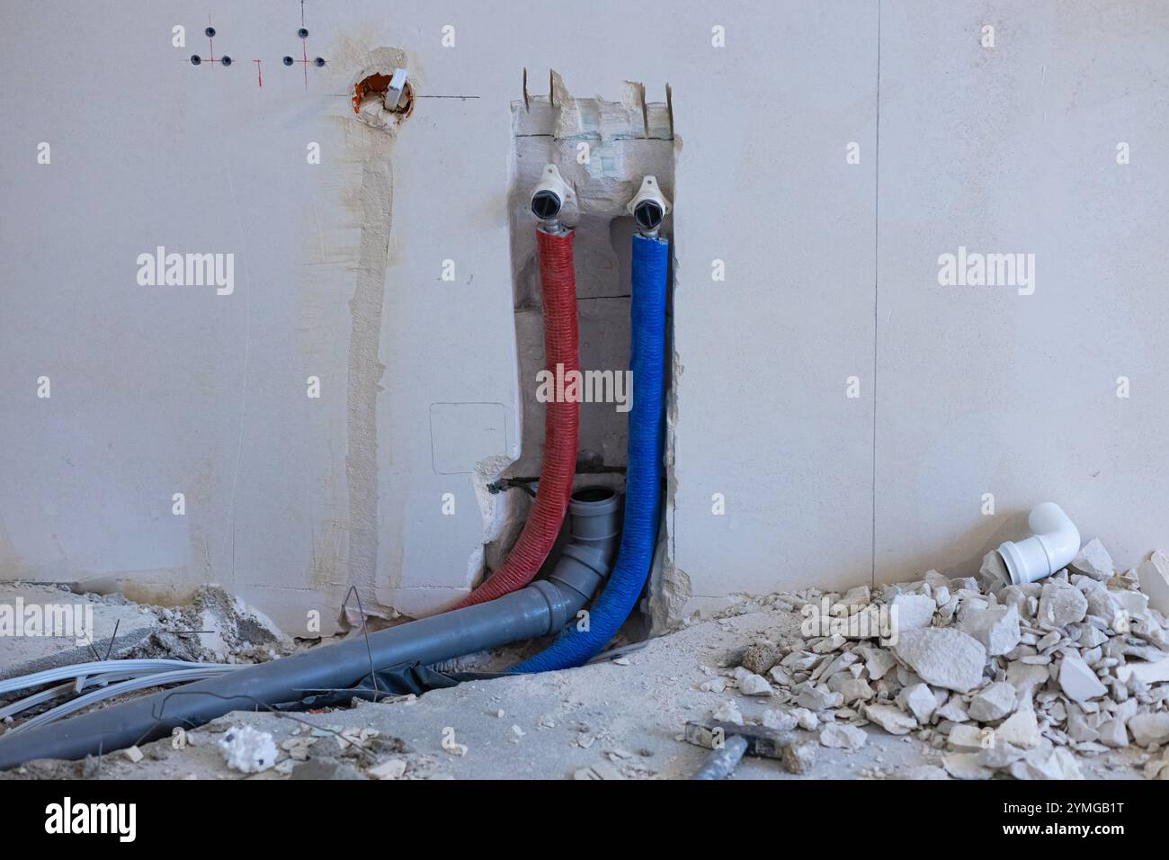 Installazione di impianti idraulici a parete con tubi dell'acqua rossi e blu esposti e componenti di drenaggio durante la ristrutturazione domestica Foto Stock