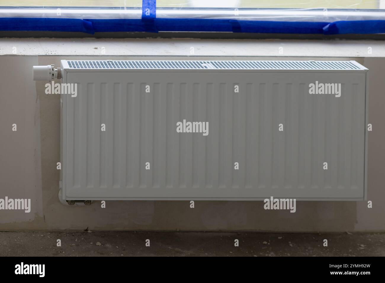 Moderno radiatore a pannello bianco installato sotto una finestra sigillata con nastro protettivo blu durante la ristrutturazione della casa Foto Stock