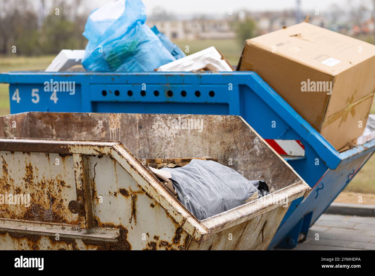 Contenitori per la spazzatura polverosi pieni di detriti e sacchetti per la spazzatura in un sito all'aperto. Smaltimento dei rifiuti e gestione dei cantieri edili Foto Stock