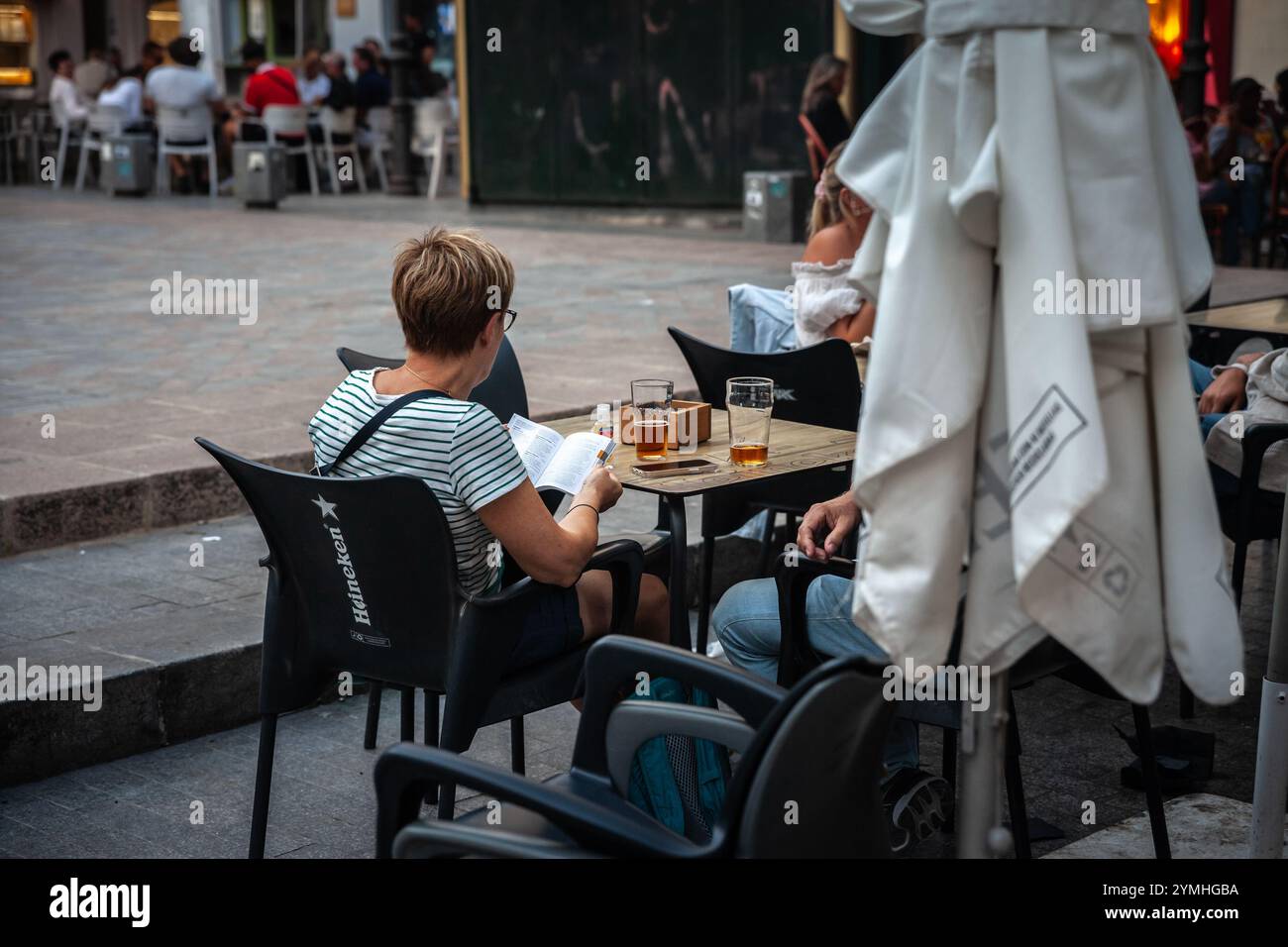 VALENCIA, SPAGNA - 13 OTTOBRE 2024: Donna, una turista, legge una guida turistica su Valencia mentre siede sulla terrazza di un caffè e beve una birra. Foto Stock