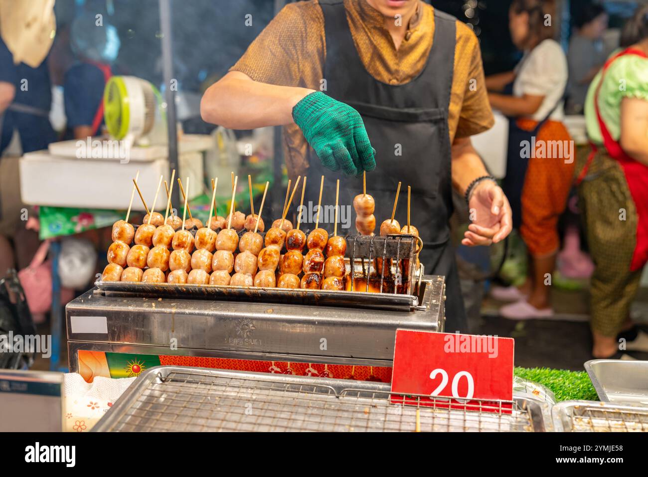 La donna sta grigliando salsicce su un piano cottura al mercato del cibo di strada. Foto Stock