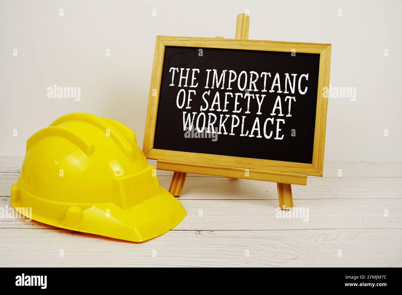 Testo sull'importanza della sicurezza sul posto di lavoro sulla lavagna con casco di sicurezza su sfondo in legno Foto Stock