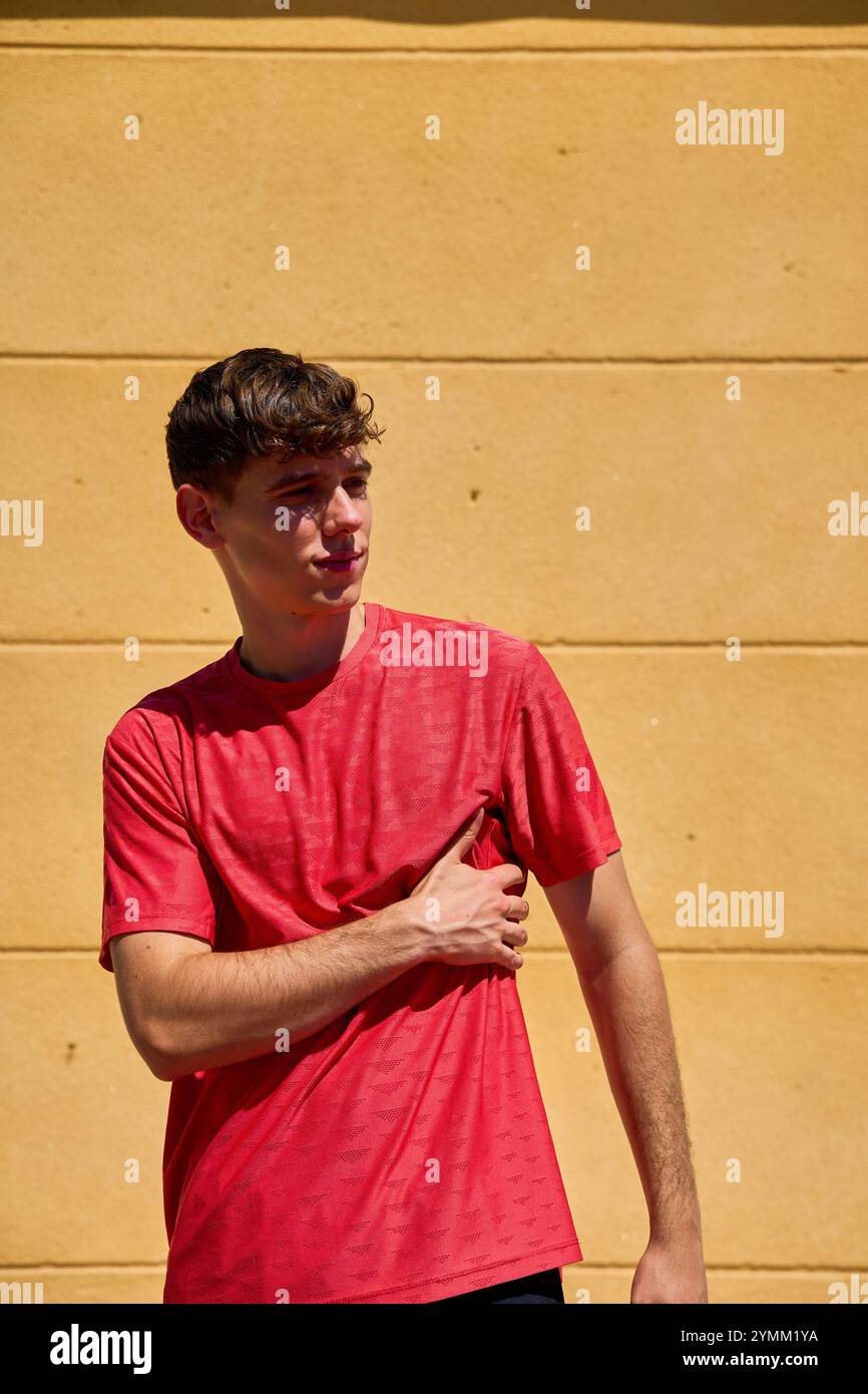 Un uomo con una camicia rossa è davanti a un muro giallo. Sta tenendo il braccio da un lato Foto Stock