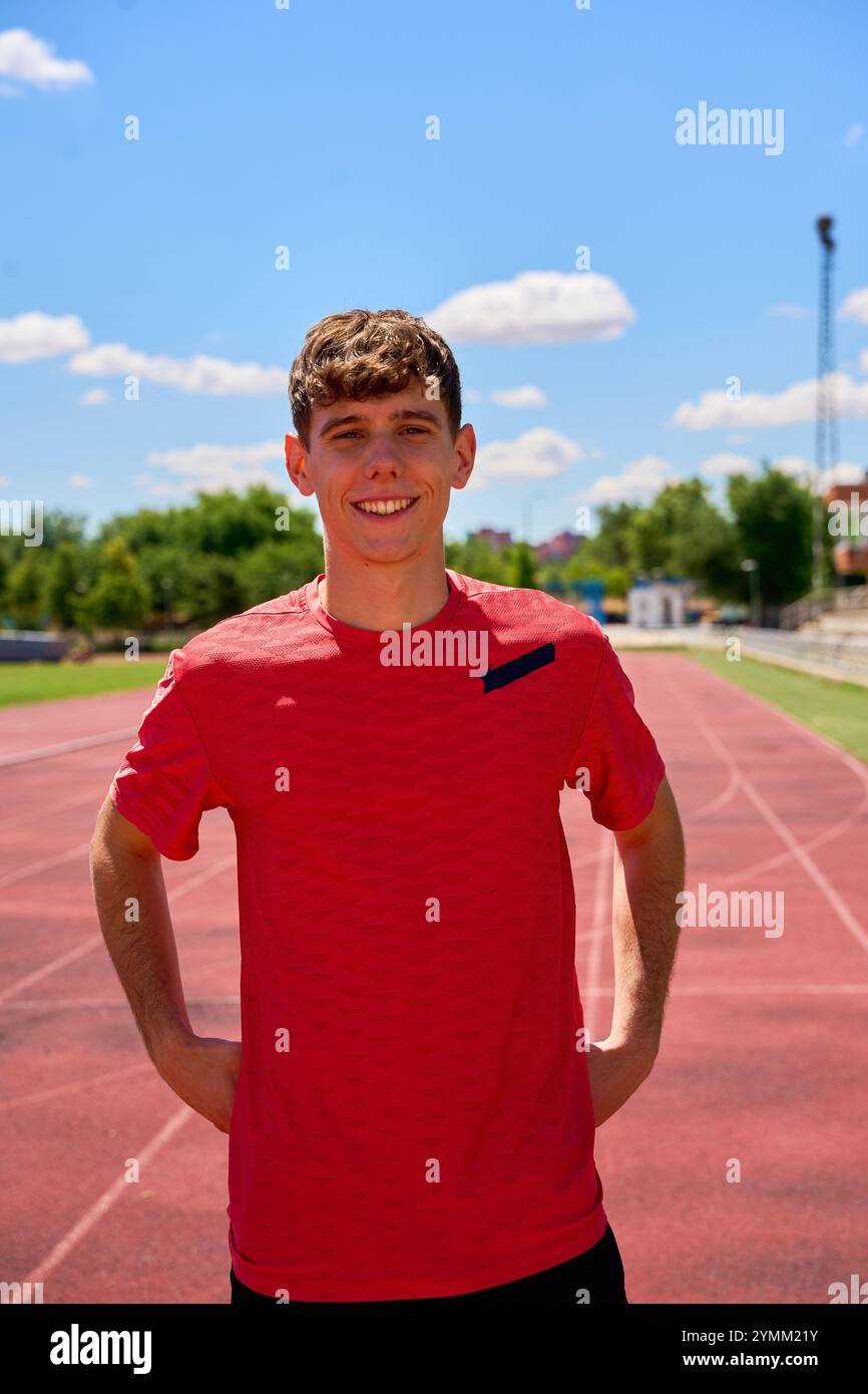 Un giovane con una maglietta rossa si trova su una pista. Sta sorridendo e posa per un film Foto Stock