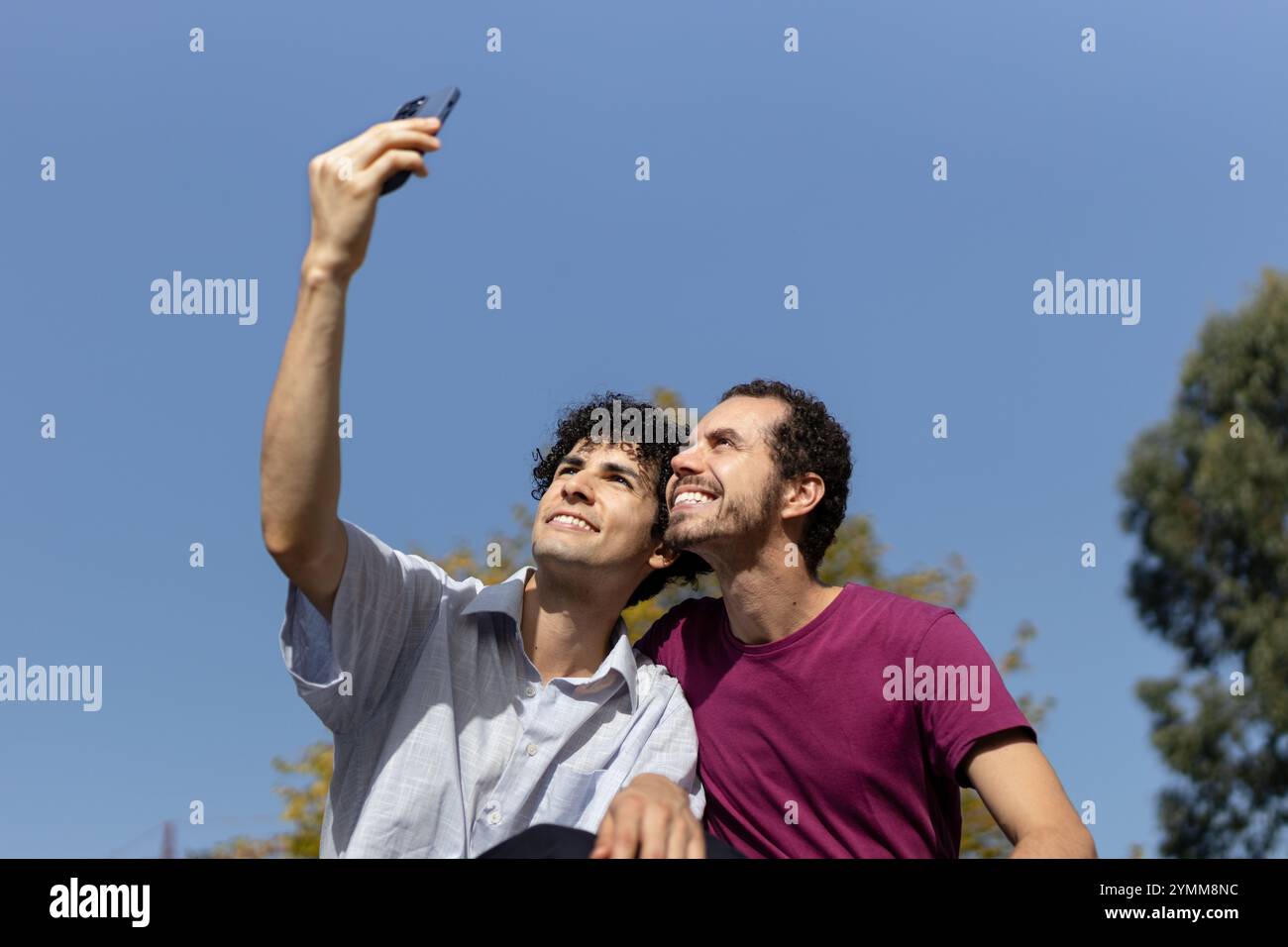 Due uomini che scattano un selfie con uno smartphone in una giornata di sole, godendosi un momento di felicità insieme. Copia spazio Foto Stock
