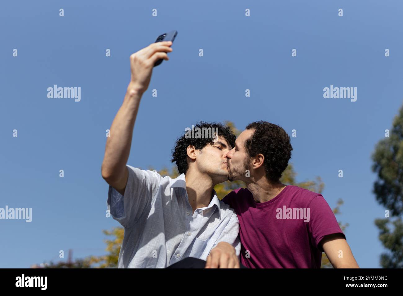 Felice coppia gay che si baciano mentre si scatta un selfie con uno smartphone all'aperto. Copia spazio Foto Stock