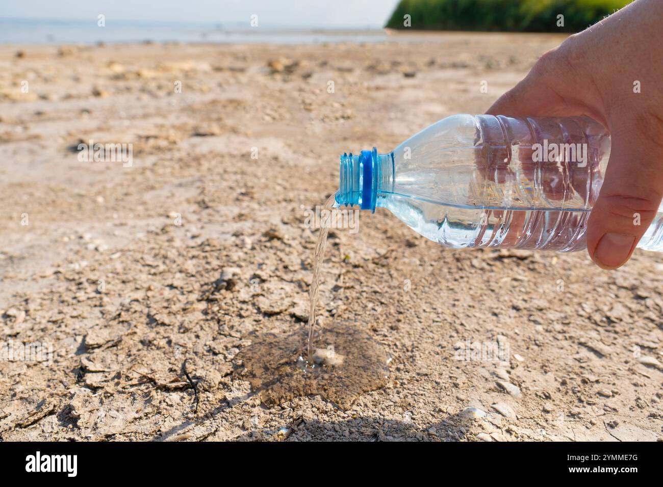 Primo piano di una bottiglia di plastica. L'acqua fuoriesce dalla bottiglia sulla superficie asciutta del fondo di un lago essiccato. Concetto di cambiamento climatico Foto Stock