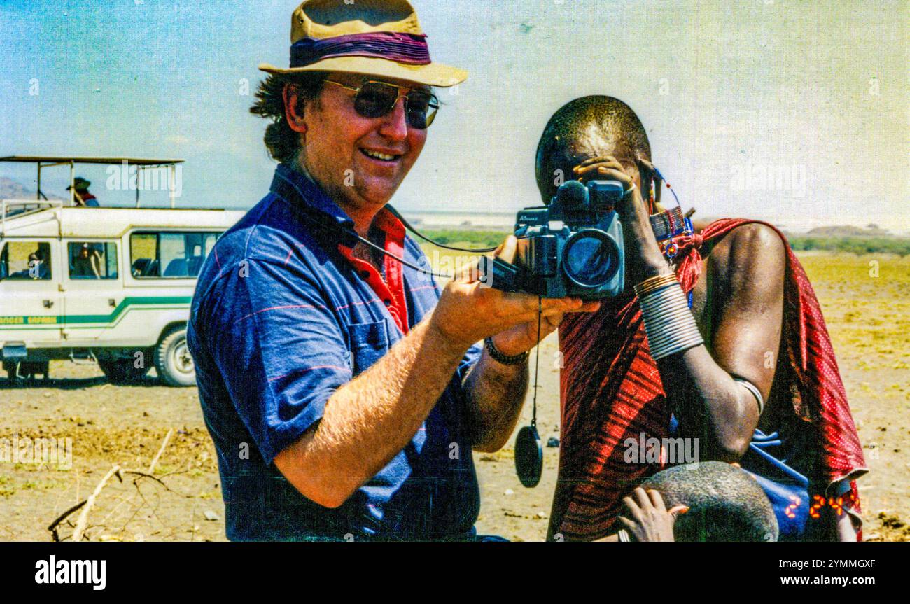 Turista caucasico che mostra una videocamera a una persona maasai con un tradizionale indumento rosso in tanzania, africa Foto Stock