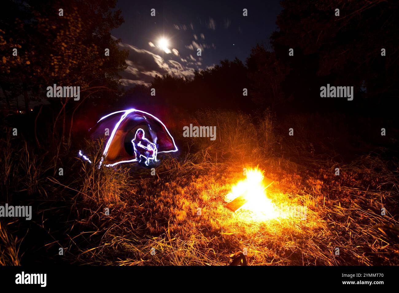 Un dipinto leggero di una tenda e una figura accanto a un falò e alla luna piena nel Montana. Questo look si ottiene con le luci lampeggianti. Foto Stock