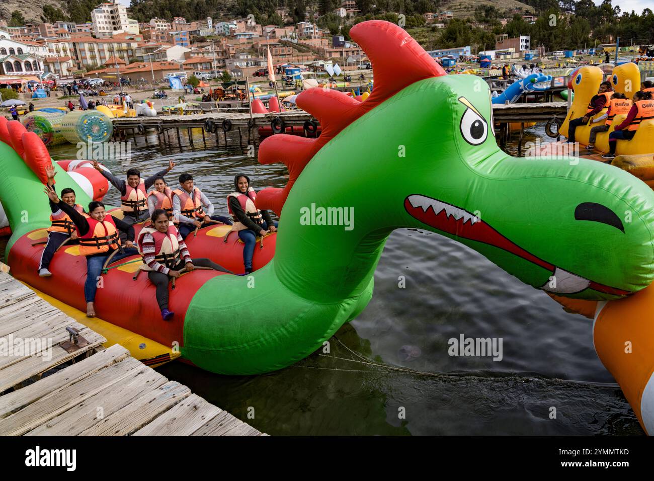 I turisti si godono un giro su un colorato drago gonfiabile sul lago titicaca, con la città di puno sullo sfondo Foto Stock