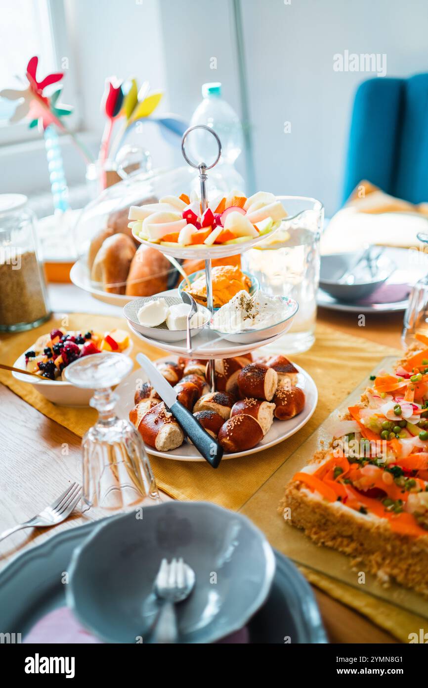 Una colazione perfettamente organizzata con un piatto di frutta, pasticcini e pretzel sul tavolo da pranzo illuminato dalla luce del sole. Perfetto per le riunioni Foto Stock