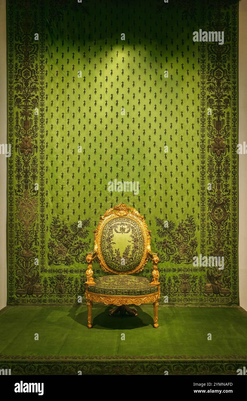 Sedia barocca decorata con struttura in oro e tappezzeria damascata verde, adagiata su una parete damascata verde coordinata, utilizzata nella cerimonia del bacio a mano. Foto Stock
