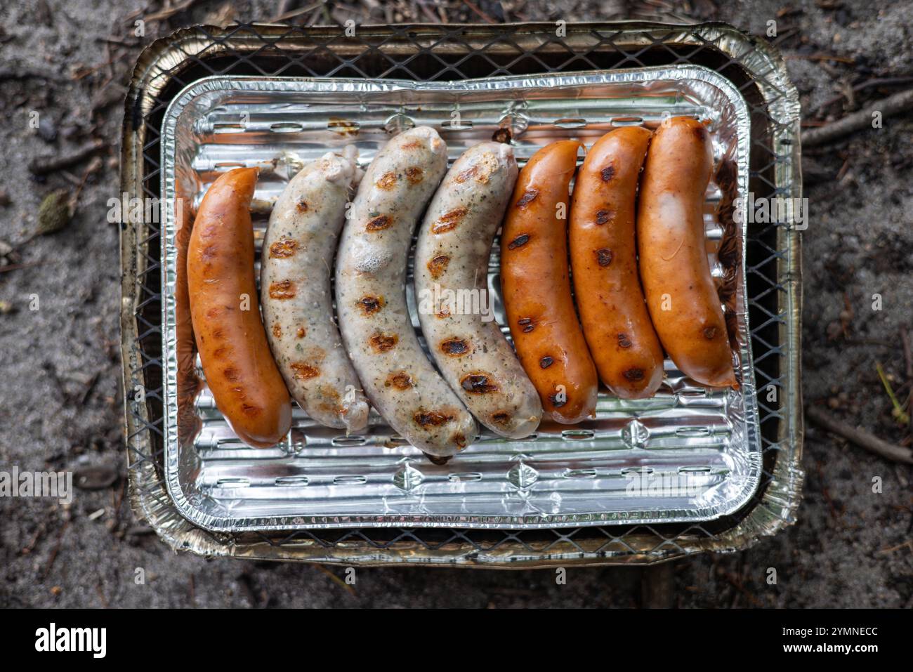 Salsicce di diversi colori vengono fritte sulla griglia di un grill usa e getta. Foto Stock