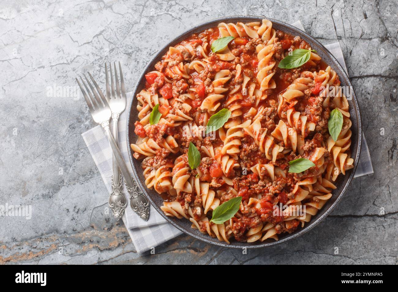 Fusilloni italiani o fusilli grandi con salsa alla bolognese da vicino in un piatto sul tavolo. Vista dall'alto orizzontale Foto Stock