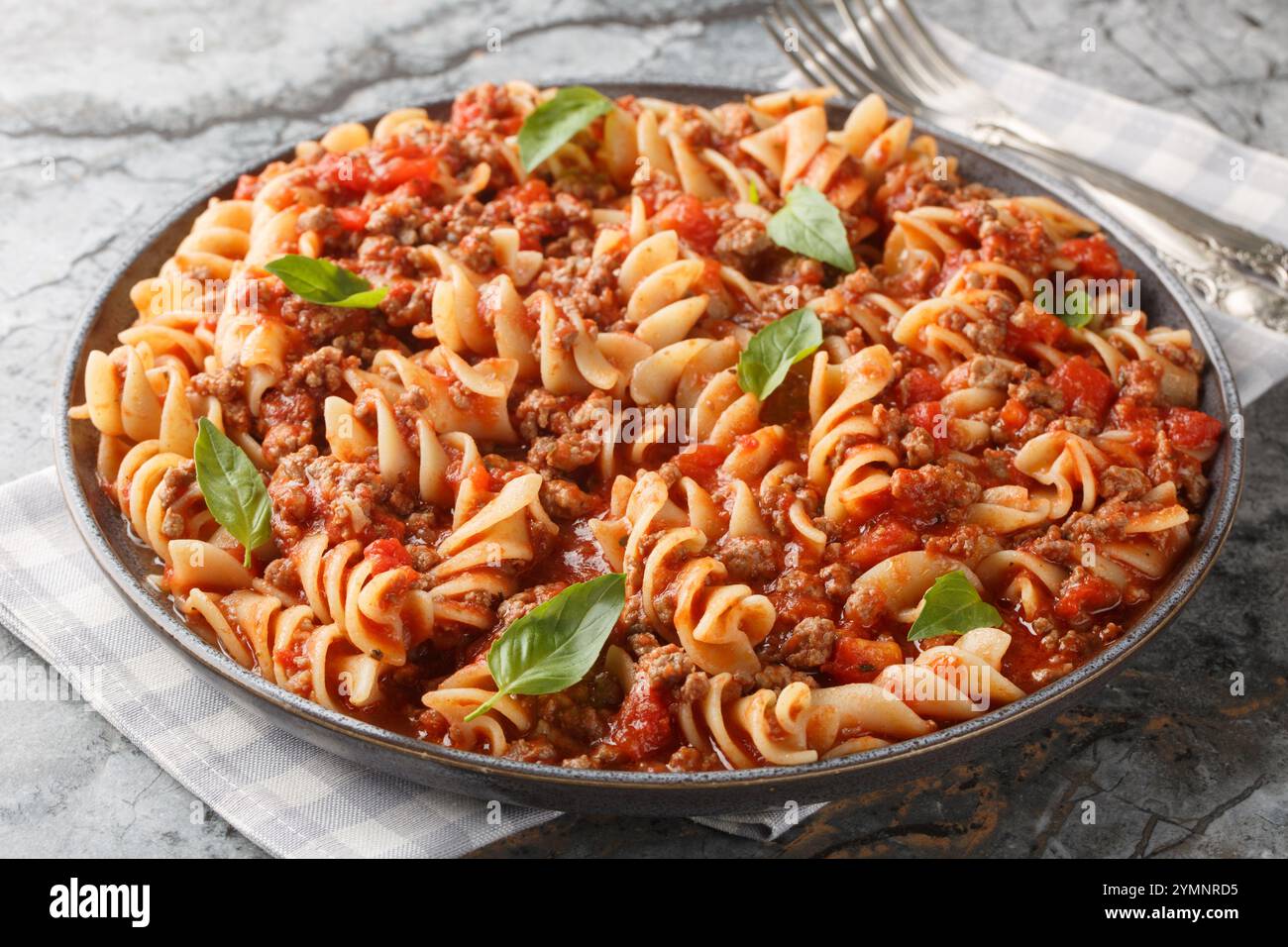 Fusilloni italiani o fusilli grandi con salsa alla bolognese da vicino in un piatto sul tavolo. Orizzontale Foto Stock