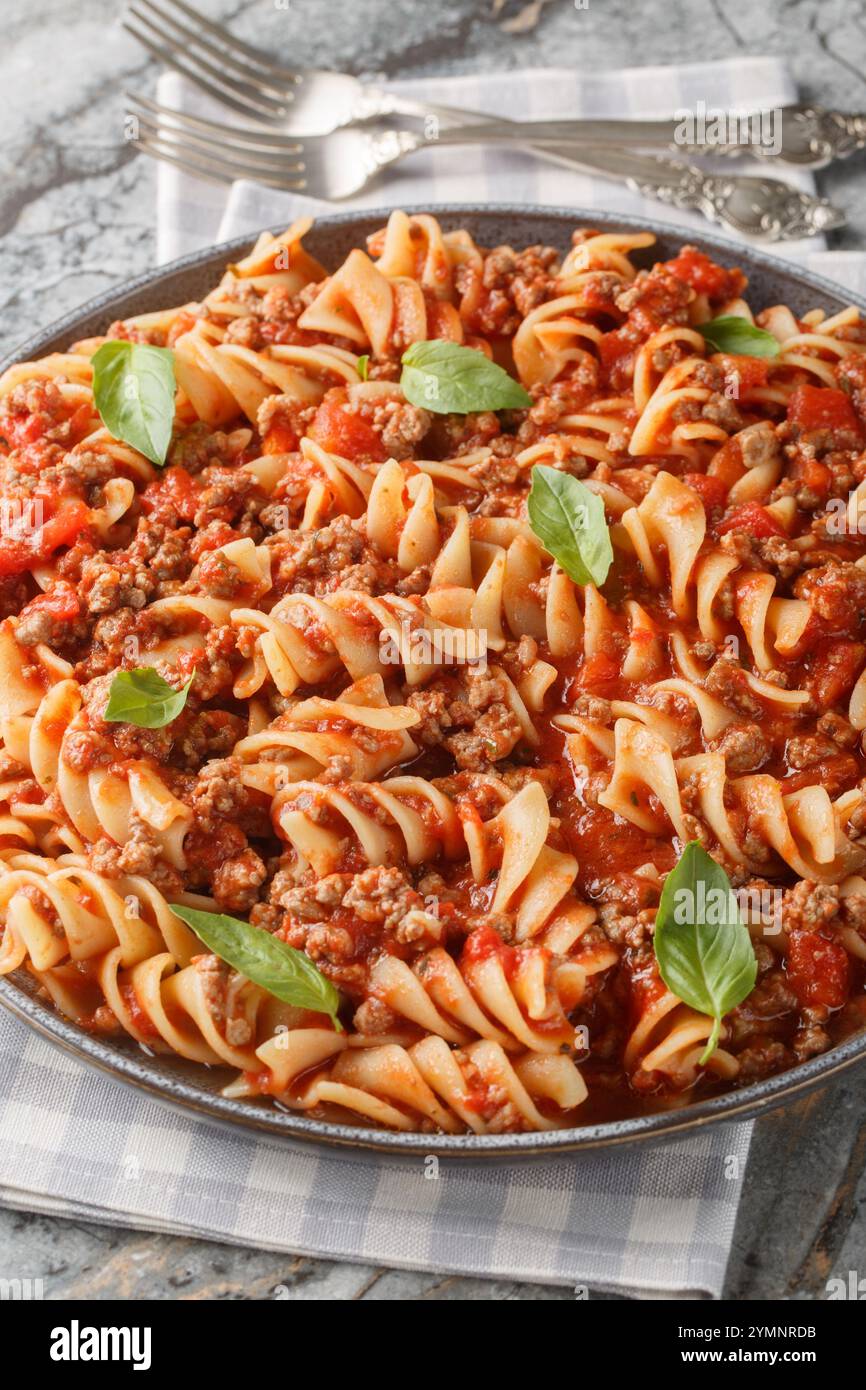 Fusilloni alla bolognese con un sostanzioso sugo di carne primo piano sul piatto del tavolo. Verticale Foto Stock