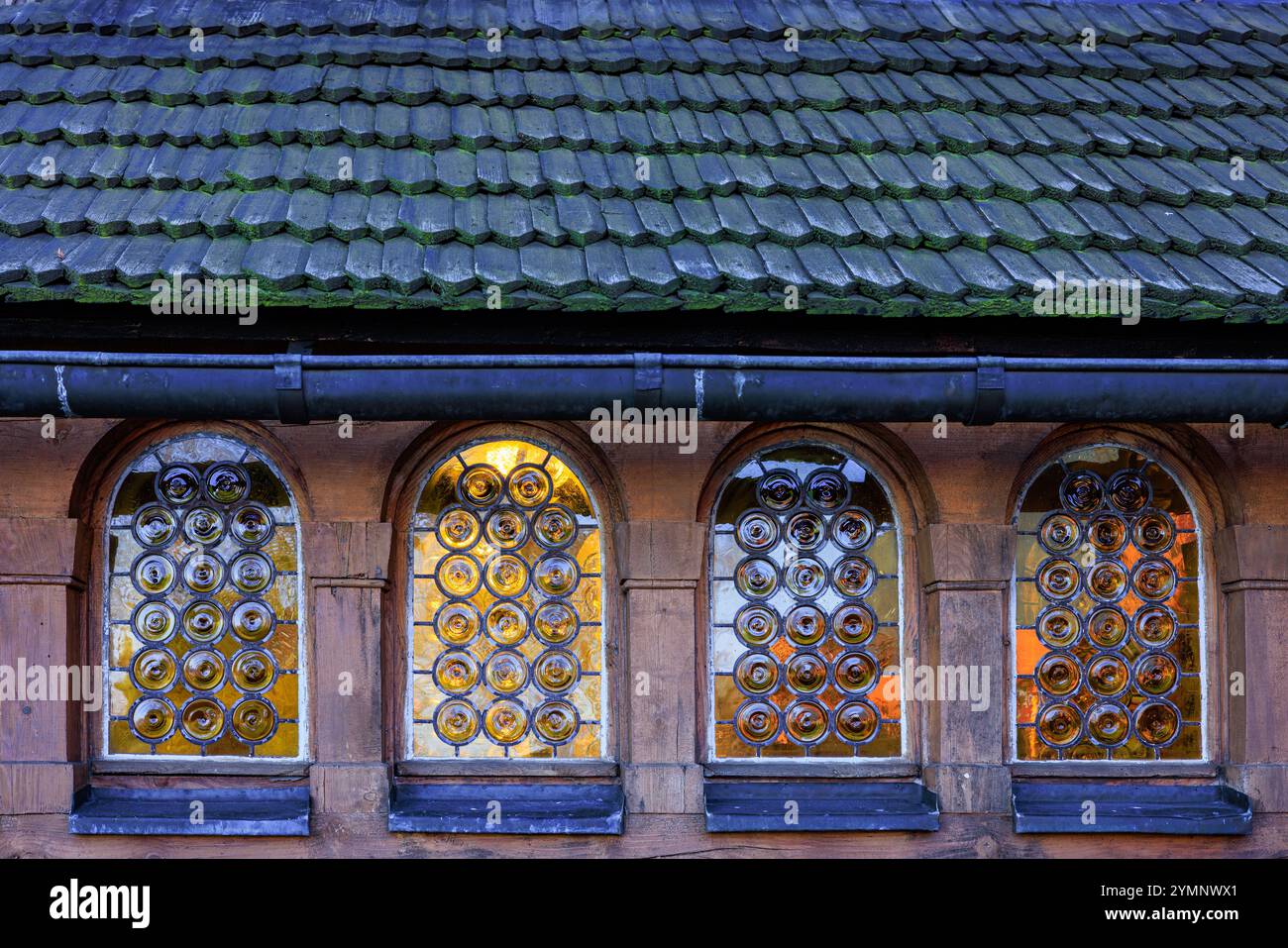 Quattro finestre ad arco di un'antica chiesa in legno con vetrate colorate gialle. Tetto piastrellato in legno. Foto Stock